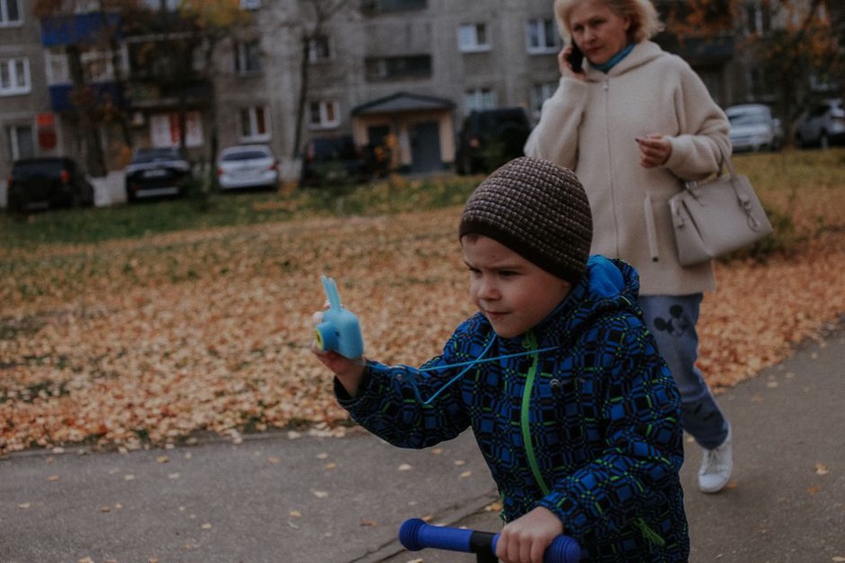 ребёнок в шлеме катится по сухой осенней дорожке